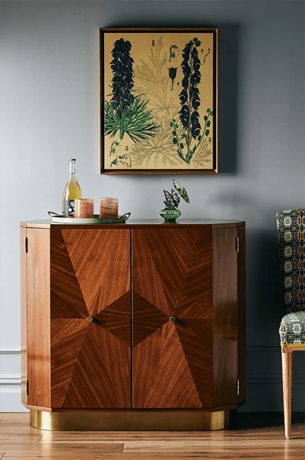 A wood-veneer-lined bar cabinet topped with glassware and a small plant
