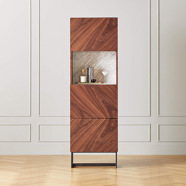 A tall bar cabinet with three closed cabinets and one barware-filled open storage cubby