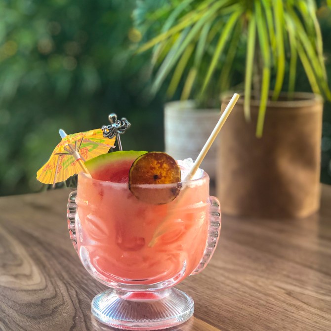 A glass tiki mug filled with fruit and a cocktail umbrella