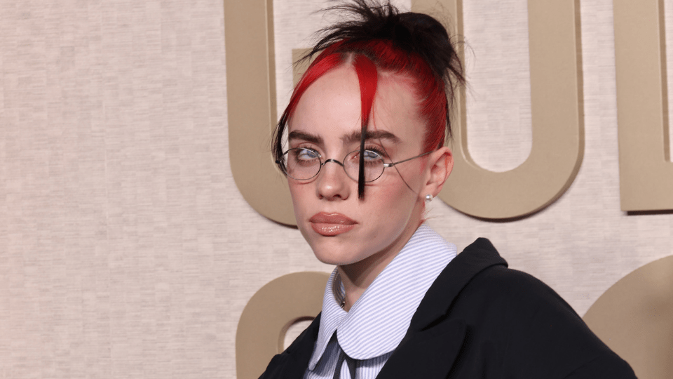 Billie Eilish in a messy bun, skinny glasses, and collared shirt at the Golden Globes