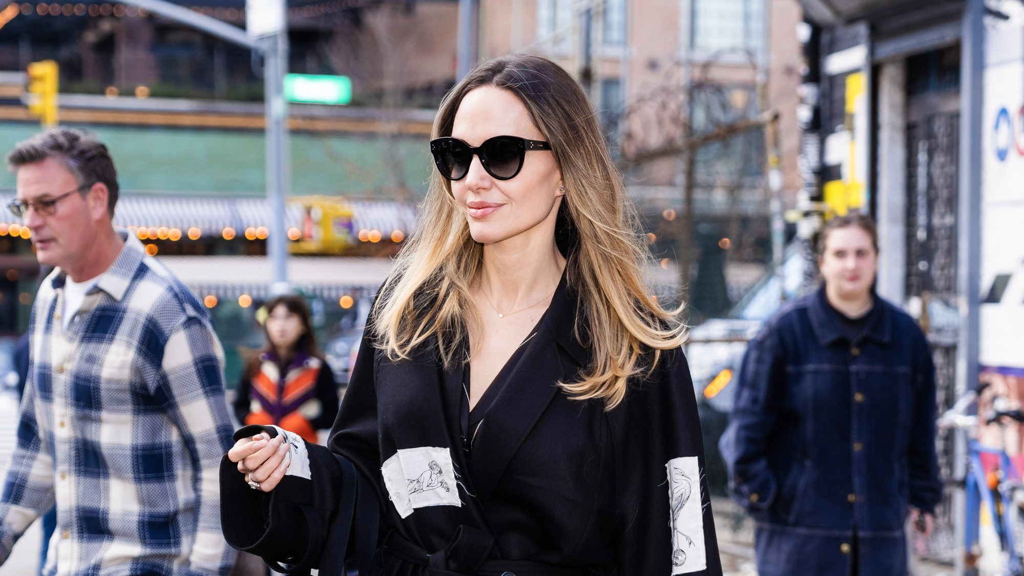 Angelina Jolie with blonde-ish hair, walking in New York City wearing sunglasses and a coat