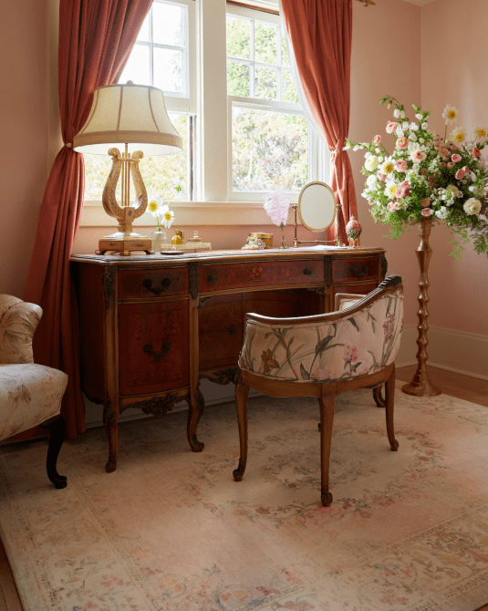 A Regency-style room with antique furniture and a light pink printed area rug