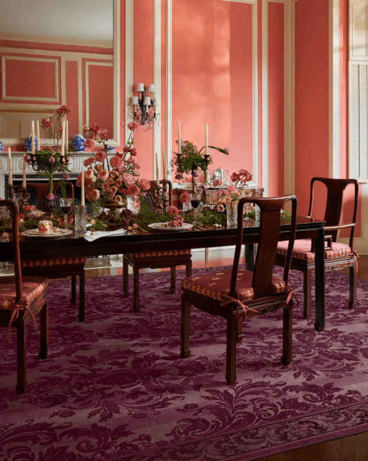 A Regency-inspired dining room with bright pink walls, antique furniture, and a purple printed rug