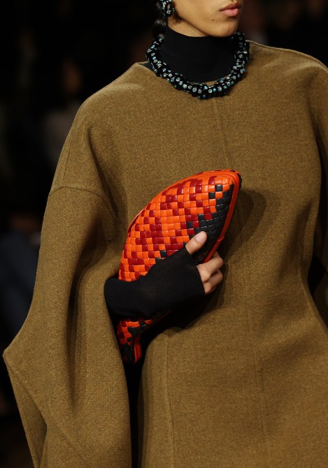 A model carrying a red woven fish clutch on the Bottega AW24 runway