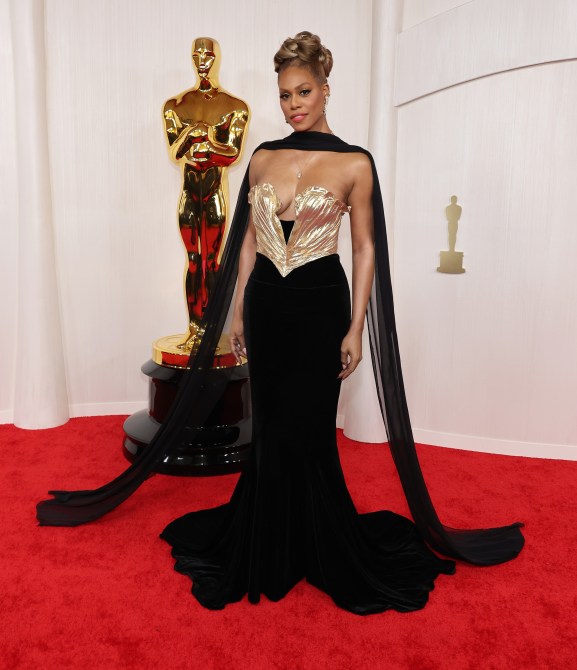 Laverne Cox in a black gown with a gold bustier and a matching black shawl at the 2024 Oscars red carpet