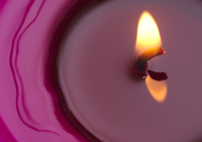 Pink candle burning with a flame at its center of pooling wax during a ritual