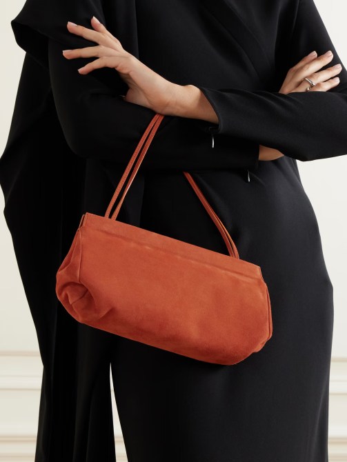 A model carries a terra cotta baguette bag with thin straps.