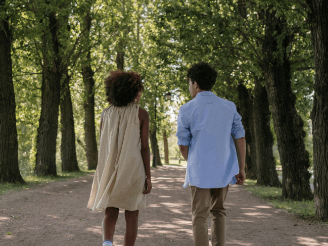 A young couple walk together down a path. The girl is in a flowy dress and boy is in a blue shirt.