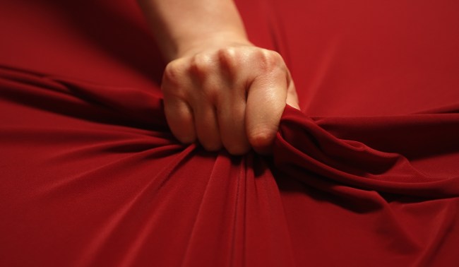 Woman hand passionately squeezes red bed sheet during orgasm.