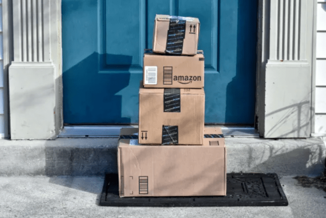 Amazon boxes piled on top of each other on a front porch in front of a blue door.
