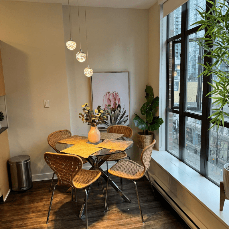 A dining room area with a dining table and four chairs and a ceiling light fixture next to a big window. A downtown Vancouver Airbnb.