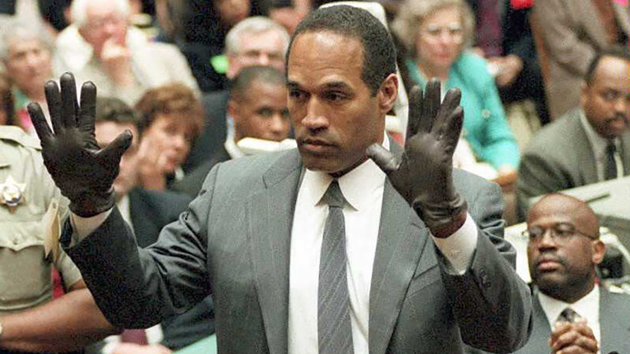 LOS ANGELES, CA - JUNE 21: O.J. Simpson shows the jury a new pair of Aris extra-large gloves, similar to the gloves found at the Bundy and Rockingham crime scene 21 June during his double murder trial in Los Angeles. Depety Sheriff Roland Jex(L) and Prosector Christopher Darden(R) look on.