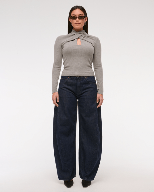 A model wearing the Abercrombie & Fitch Curve Love Mid Rise Ultra Barrel Jean in a dark denim wash